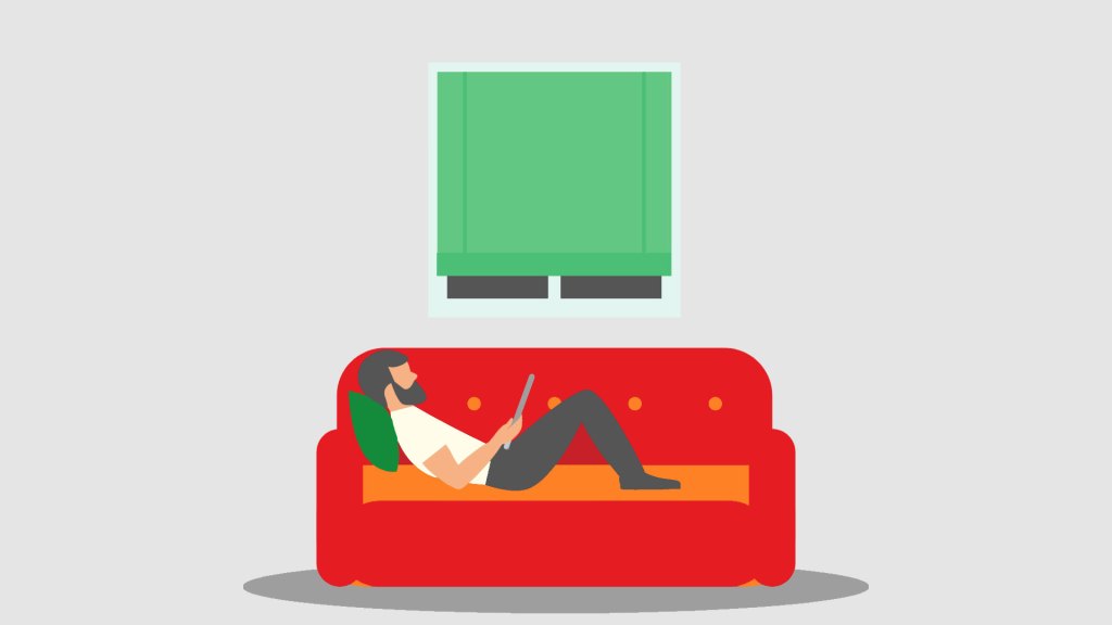 A man is lying on a red sofa while working from home. Green pillow and window 