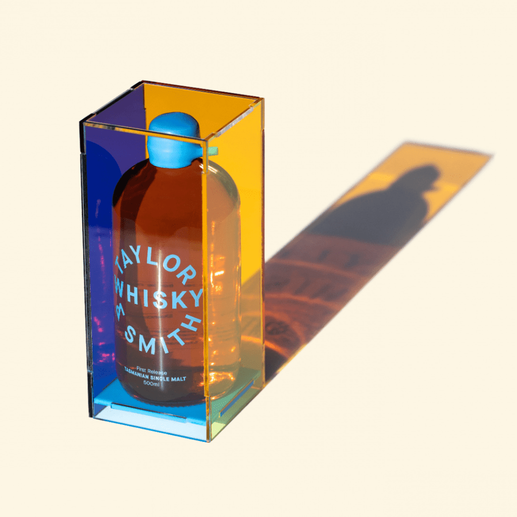 The whiskey comes in a round, glass bottle with a light blue cap. Outside the bottle is an amber colored clear acrylic case.
