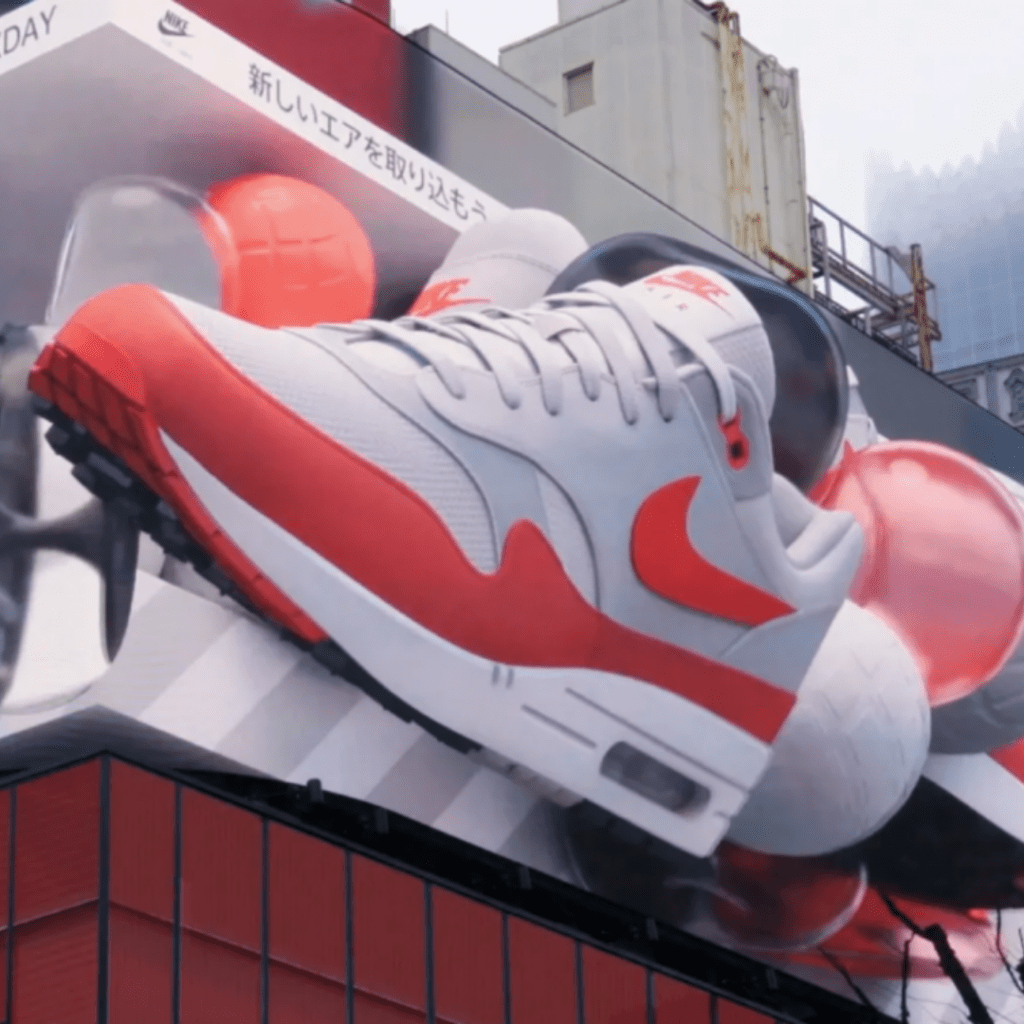 A giant pair of Nike Air Max sneakers pops out of a 3D billboard. 